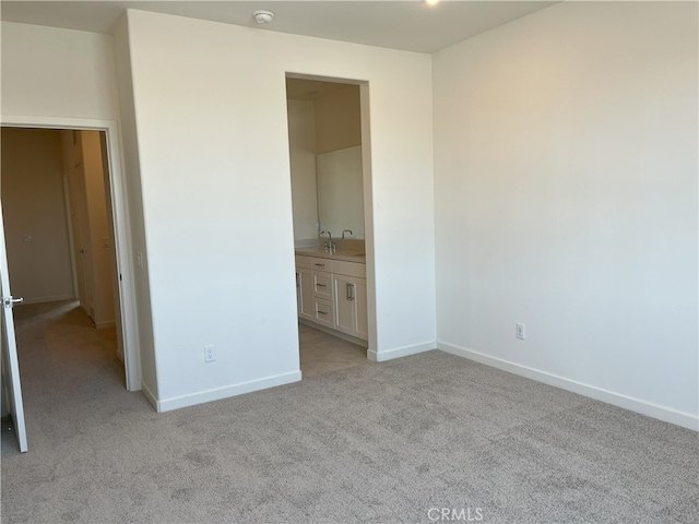 unfurnished bedroom with light colored carpet, baseboards, a sink, and ensuite bath