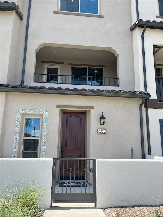 property entrance featuring stucco siding, fence, and a balcony