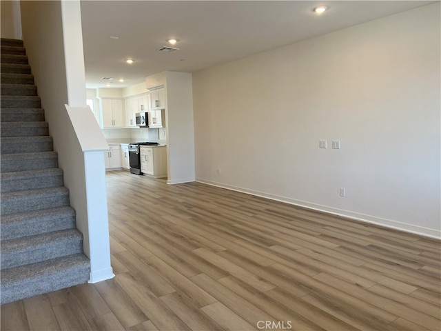 unfurnished living room with light wood finished floors, stairway, baseboards, and recessed lighting