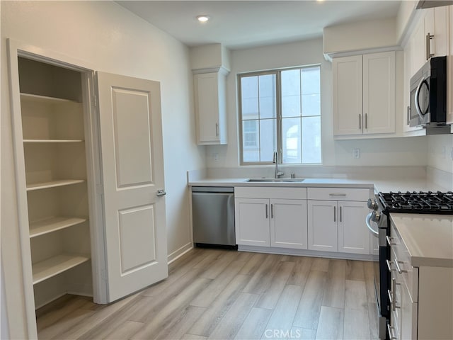 kitchen with a sink, stainless steel appliances, white cabinets, light wood-style flooring, and light countertops