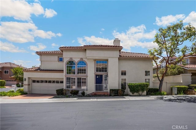 mediterranean / spanish home with a chimney, stucco siding, driveway, a tiled roof, and an attached garage