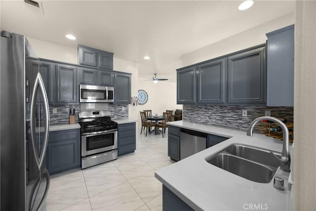 kitchen with appliances with stainless steel finishes, a sink, decorative backsplash, a ceiling fan, and light marble finish flooring