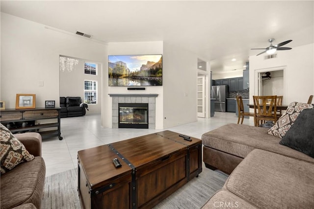 living area with a ceiling fan, a tile fireplace, and light tile patterned flooring