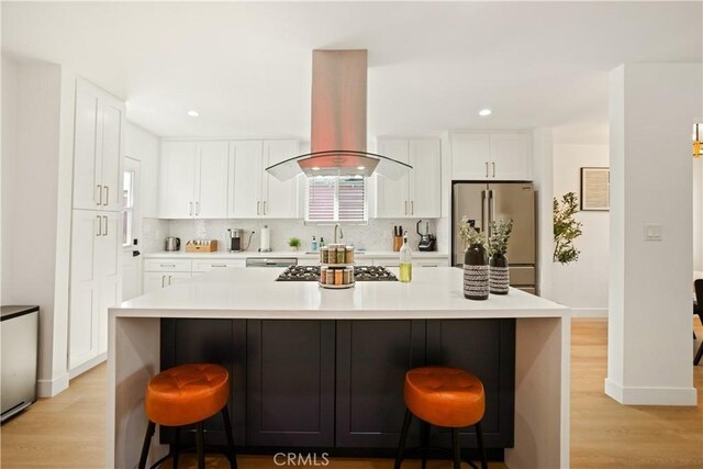 6916 Etiwanda Ave, Reseda, CA 91335 - kitchen with appliances with stainless steel finishes, island exhaust hood, light wood-type flooring, decorative backsplash, and a breakfast bar area