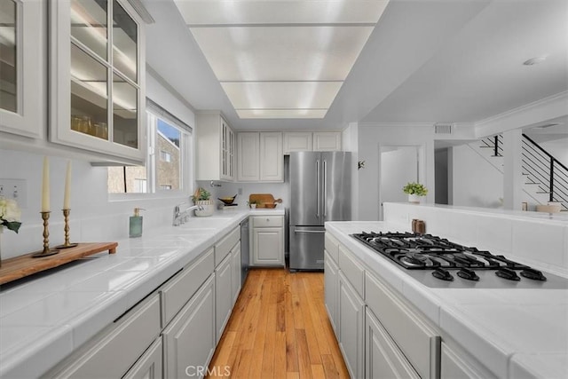 1006 Palm Ln, Redondo Beach, CA 90278 - kitchen with stainless steel appliances, tile counters, light wood-type flooring, a sink, and white cabinetry