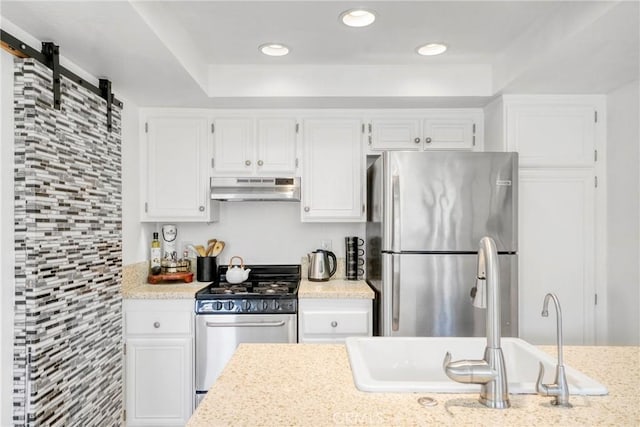 kitchen featuring stainless steel appliances, under cabinet range hood, a sink, white cabinets, and recessed lighting