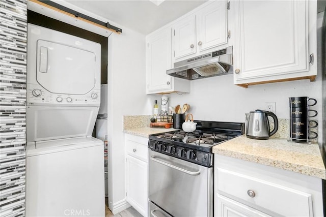 kitchen with under cabinet range hood, gas range, stacked washer / dryer, and white cabinetry