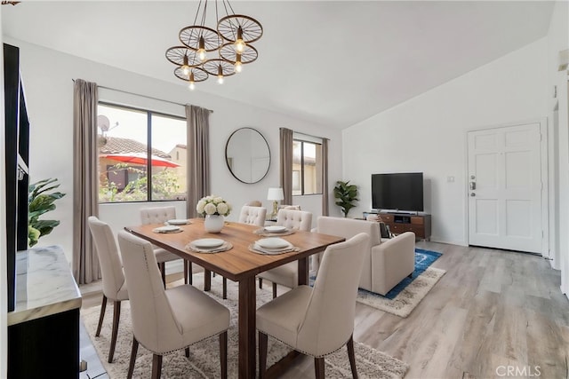 dining area featuring vaulted ceiling, plenty of natural light, a chandelier, and light wood-style floors