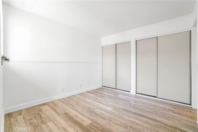 unfurnished bedroom featuring two closets, wood finished floors, and baseboards