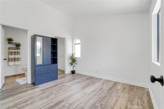 unfurnished bedroom featuring light wood-type flooring, baseboards, connected bathroom, and a walk in closet
