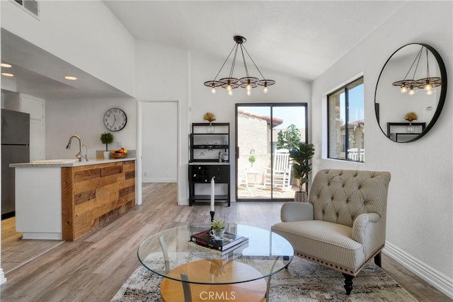 living area with a chandelier, light wood-style flooring, lofted ceiling, and baseboards