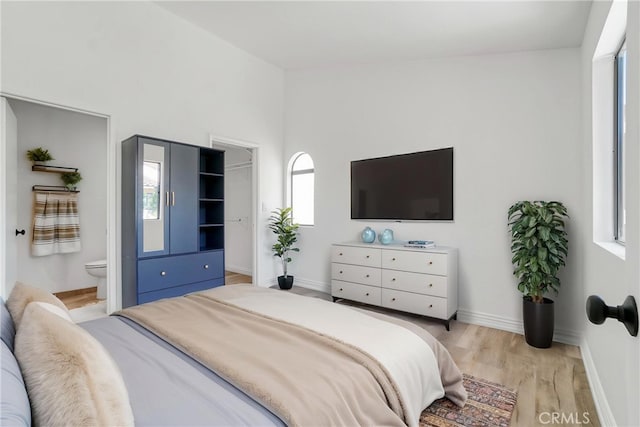bedroom with light wood-style flooring, baseboards, and connected bathroom