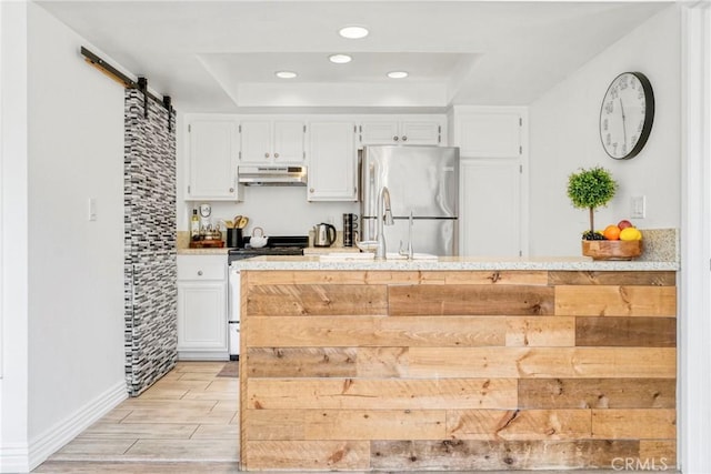 kitchen with range with gas stovetop, freestanding refrigerator, under cabinet range hood, a barn door, and light wood-style floors