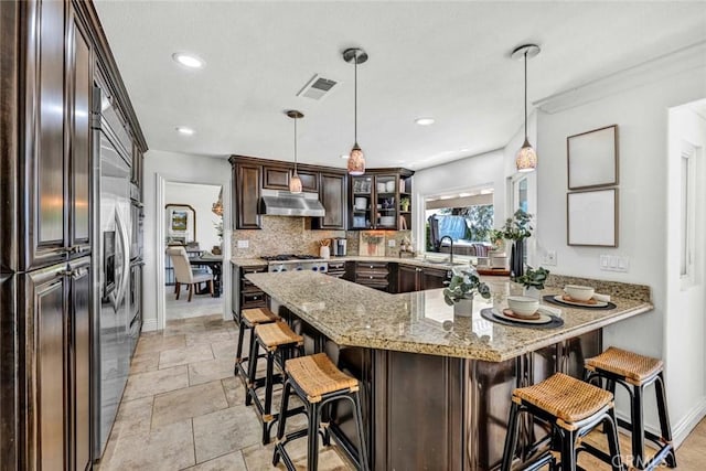 6142 E E W View Dr, Orange, CA 92869 - kitchen with under cabinet range hood, built in refrigerator, dark brown cabinetry, a kitchen breakfast bar, and light stone countertops