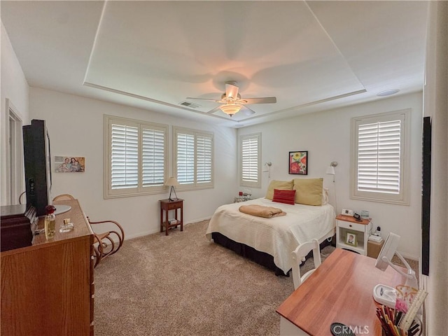 carpeted bedroom with a raised ceiling, baseboards, and ceiling fan