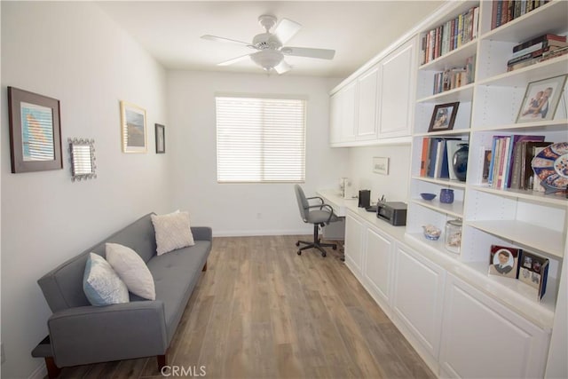 office featuring built in desk, a ceiling fan, light wood-style floors, and baseboards