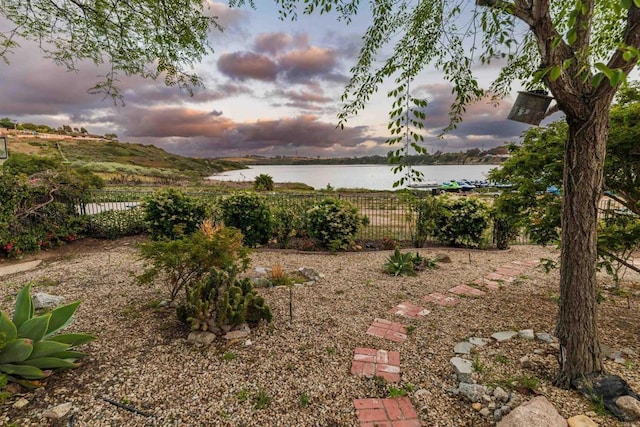 yard at dusk featuring fence and a water view