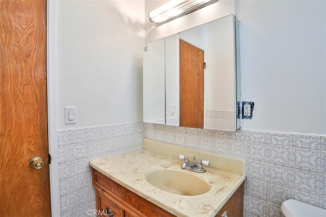 half bathroom with tile walls, vanity, toilet, and wainscoting