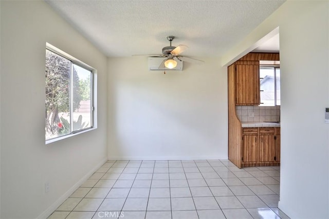 unfurnished dining area with a textured ceiling, ceiling fan, light tile patterned floors, and baseboards