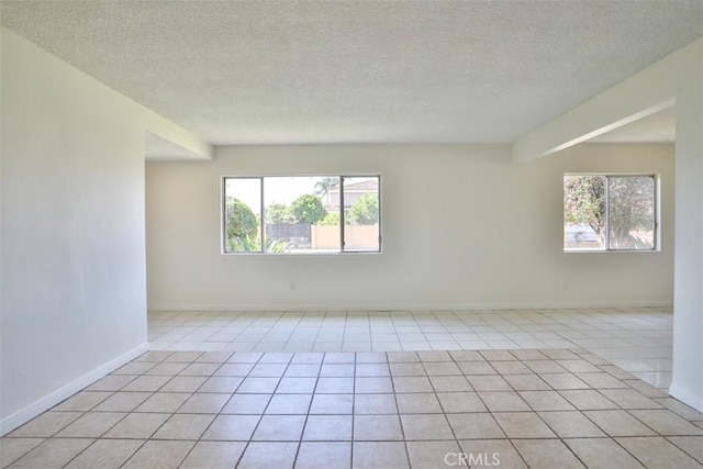 empty room featuring light tile patterned floors, a textured ceiling, and baseboards