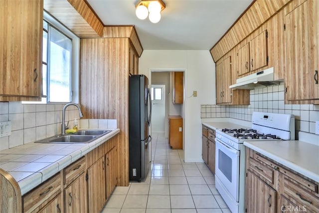 kitchen featuring gas range gas stove, under cabinet range hood, freestanding refrigerator, a sink, and light tile patterned floors