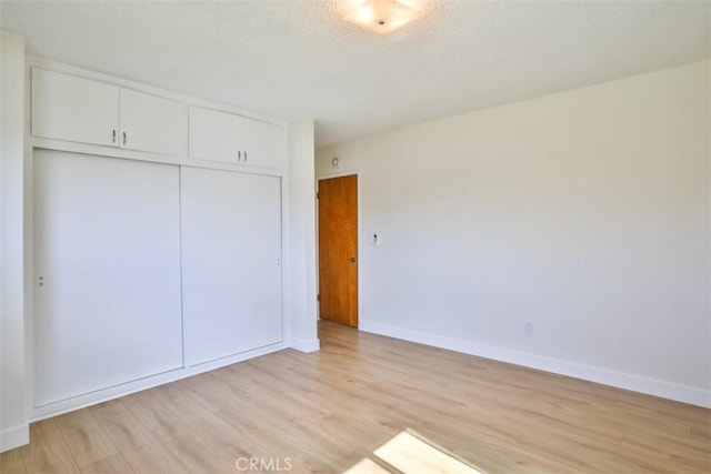 unfurnished bedroom featuring light wood finished floors, baseboards, and a closet