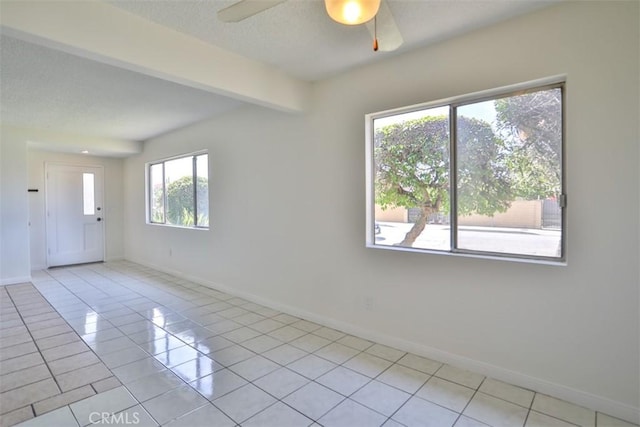 spare room featuring baseboards, ceiling fan, light tile patterned floors, and a textured ceiling