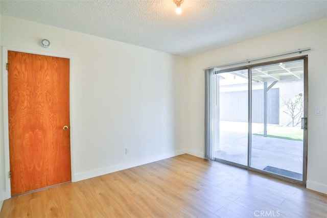 spare room with light wood-style floors, a textured ceiling, and baseboards