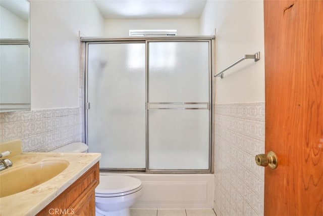 bathroom with toilet, tile patterned floors, a wainscoted wall, vanity, and bath / shower combo with glass door
