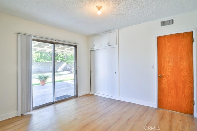 unfurnished bedroom with access to exterior, light wood finished floors, a textured ceiling, baseboards, and a closet