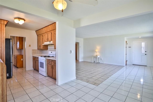 kitchen featuring white range with gas stovetop, freestanding refrigerator, light tile patterned flooring, light countertops, and backsplash