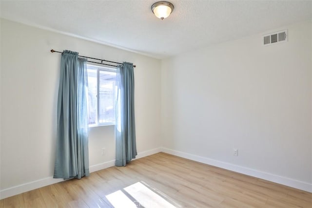 spare room with light wood-type flooring, baseboards, and a textured ceiling