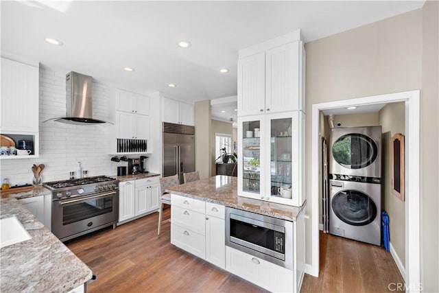 65 Centre Ct, Dana Point, CA 92629 - kitchen with wall chimney exhaust hood, built in appliances, stacked washer and clothes dryer, backsplash, and light stone counters