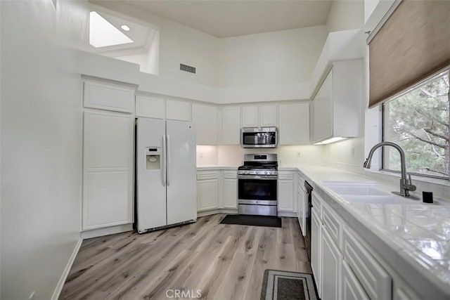 2643 Dietrich Dr, Tustin, CA 92782 - kitchen featuring appliances with stainless steel finishes, white cabinets, light countertops, a towering ceiling, and light wood-type flooring