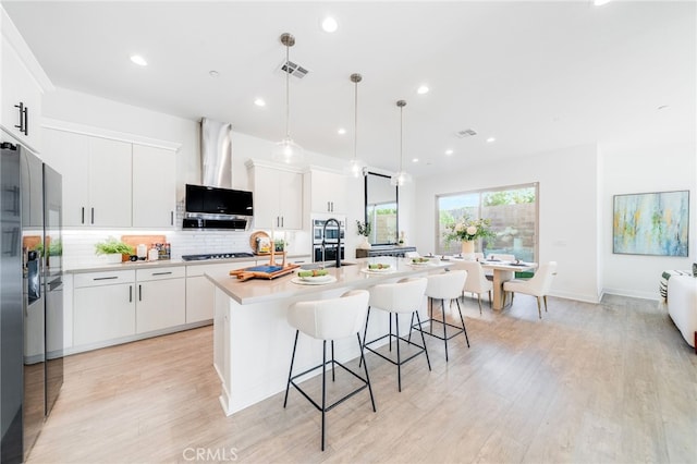 196 Episode, Irvine, CA 92618 - kitchen featuring decorative backsplash, light wood-style floors, a kitchen bar, a kitchen island with sink, and stainless steel fridge with ice dispenser