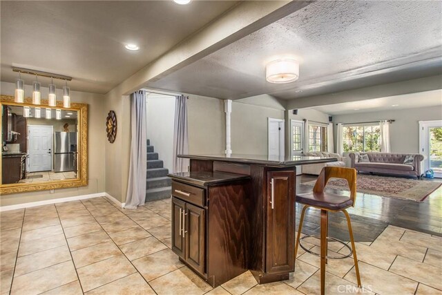 11425 Bryant St, Yucaipa, CA 92399 - kitchen featuring stainless steel fridge with ice dispenser, light tile patterned floors, dark countertops, a breakfast bar, and dark brown cabinets