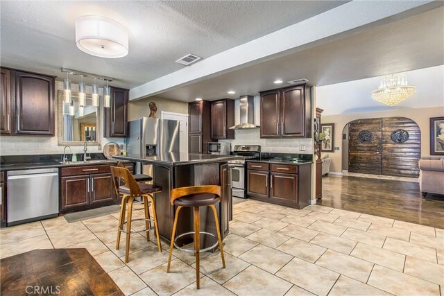 11425 Bryant St, Yucaipa, CA 92399 - kitchen with stainless steel appliances, dark countertops, wall chimney range hood, arched walkways, and a textured ceiling