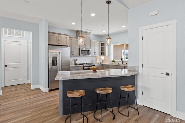 kitchen featuring appliances with stainless steel finishes, a kitchen bar, a peninsula, a sink, and light stone counters