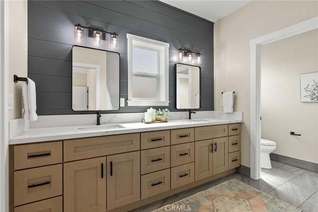 bathroom with toilet, double vanity, baseboards, and marble look tiles