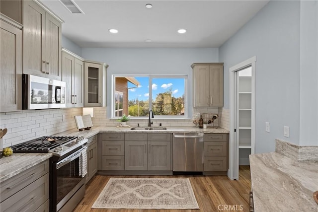 kitchen featuring appliances with stainless steel finishes, a sink, light stone countertops, tasteful backsplash, and light wood-style flooring
