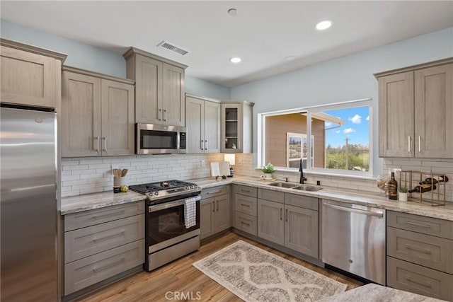 kitchen with appliances with stainless steel finishes, a sink, tasteful backsplash, light wood-type flooring, and light stone counters