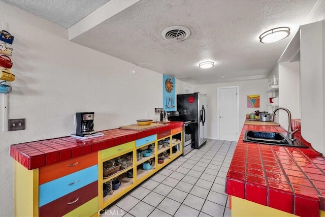 56772 Kismet Rd, Yucca Valley, CA 92284 - kitchen with appliances with stainless steel finishes, a sink, a textured ceiling, light tile patterned floors, and tile counters