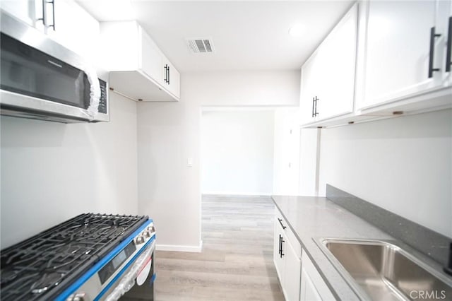 1336 W 118th St, Los Angeles, CA 90044 - kitchen featuring appliances with stainless steel finishes, white cabinets, light wood-style flooring, and a sink