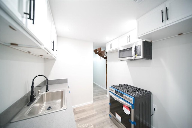 1336 W 118th St, Los Angeles, CA 90044 - kitchen featuring stainless steel appliances, a sink, light wood-style floors, white cabinetry, and baseboards