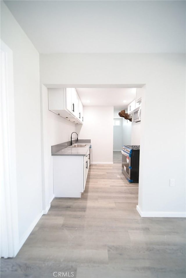 1336 W 118th St, Los Angeles, CA 90044 - kitchen featuring stainless steel appliances, a sink, white cabinets, light wood-style flooring, and baseboards