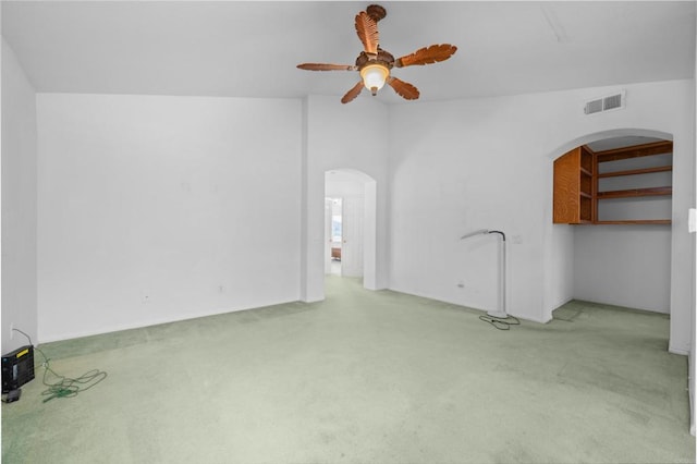 unfurnished living room featuring arched walkways, a ceiling fan, and carpet