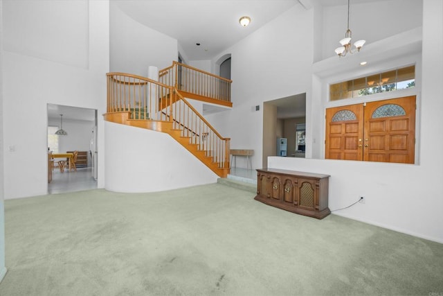 unfurnished living room with high vaulted ceiling, carpet flooring, stairs, and a chandelier