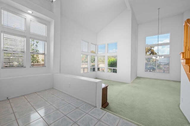 unfurnished room with high vaulted ceiling, a chandelier, light carpet, and light tile patterned flooring