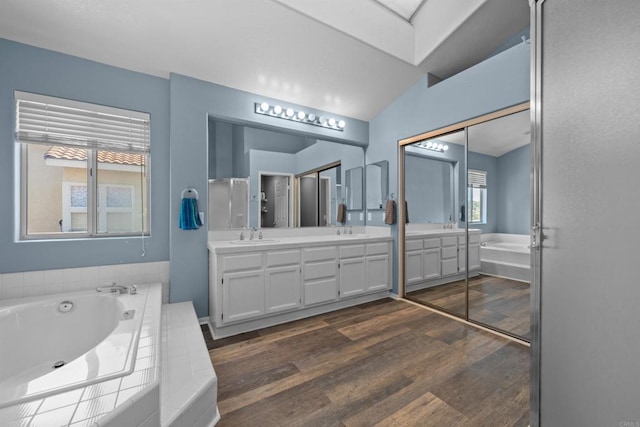 bathroom featuring a bath, double vanity, and wood finished floors