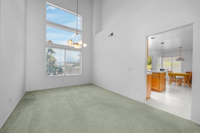 spare room featuring a chandelier, light colored carpet, and a high ceiling